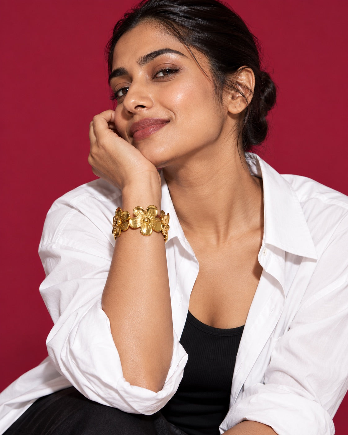 Model in a white shirt wearing the five-petal floral gold-tone cuff against a Cherry studio backdrop